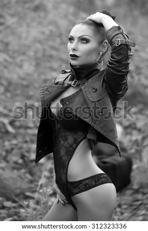 Pretty sexy brunette young wild lady with bright make-up ponytail and beautiful bottom in leather biker jacket and erotic lace lingerie on natural background black and wgite, vertical picture