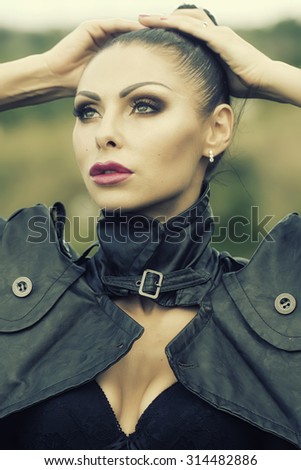 Portrait of pensive sexual brunette young wild woman with bright make-up and ponytail in black leather jacket and lace underwear looking away outdoor on natural background, vertical picture