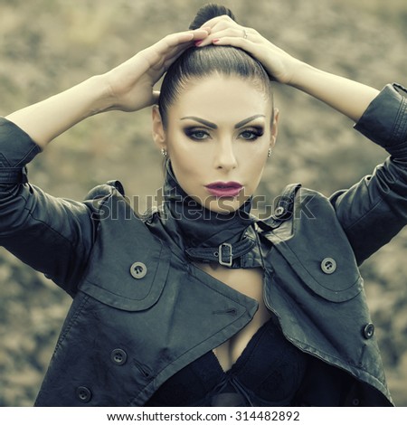 Portrait of pensive sexy brunette young wild woman with bright make-up and ponytail in black leather jacket and lace underwear looking forward outdoor on natural background, square picture
