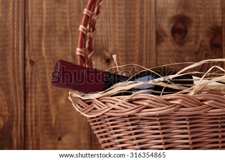 One vintage corked glass bottle of red wine with label decorated with straw lies in gift wicker basket on wooden planks wall background, horizontal photo