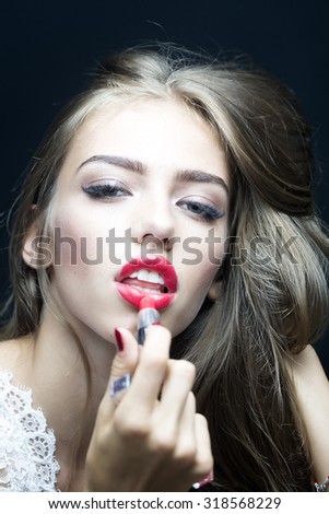 Portrait of fashionable sexy female model with lush hair putting on red lipstick on lips in white clothes from lace looking forward on black studio background closeup, vertical picture
