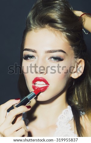 Portrait of fashionable sensory female model with lush hair putting on red lipstick on lips in white clothes from lace looking forward on black studio background closeup, vertical picture
