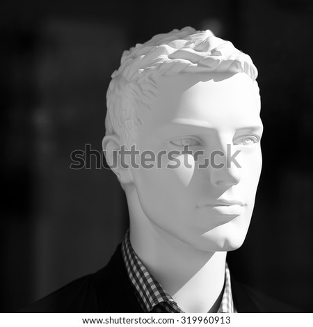 Closeup of one white realistic plastic imitating human body mannequin male face in shopping showcase standing in light on dark background, square picture