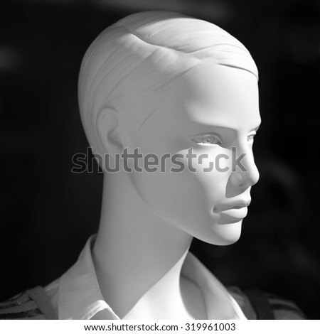 Closeup of one white realistic plastic imitating human body mannequin female face in shopping showcase standing in light on dark background, square picture