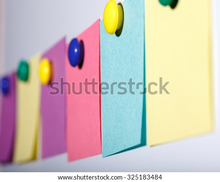 Closeup side view of six empty colorful paper stickers pink yellow violet and blue colors hanging on white flat blank wall copyspace with no people, horizontal picture