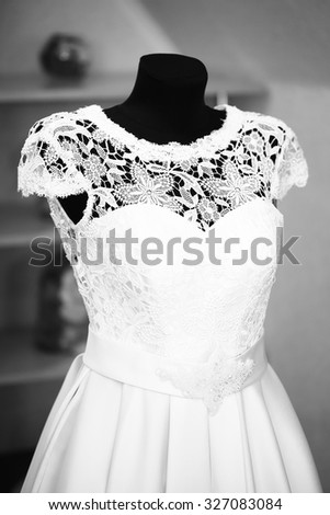One beautiful female wedding dress with upper part of lace hanging on headless mannequin indoor black and white, vertical picture