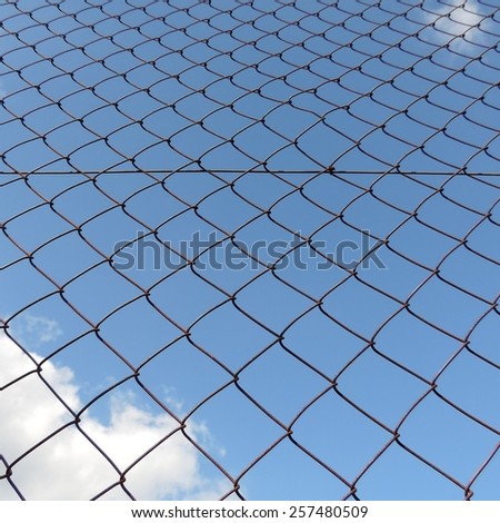Metal mesh wire fence with cloud and blue sky background