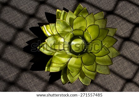 Green candle holder shaped like a spiky flower on grey material with square shadow patterns caused by sunlight streaming through a window.