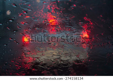 Driving at night in the rain looking at a car in front with their brake lights on distorted by the rain on the windshield.