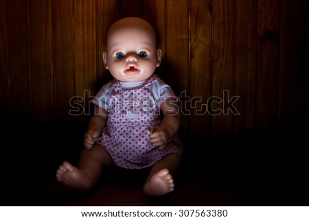 Scary photo of a doll lit from below and with heavy shadow to create atmosphere with a wooden background.
