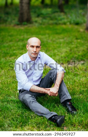 Portrait of a bald and brutal man. Bald guy sitting on the grass in the park.