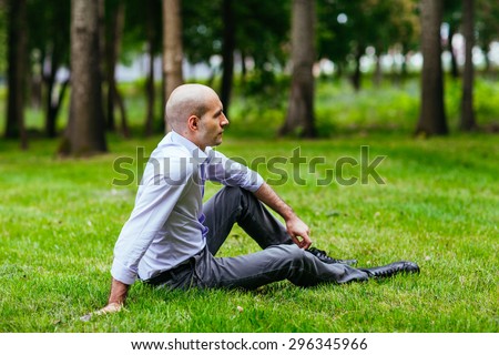 Portrait of a bald and brutal man. Bald guy sitting on the grass in the park.
