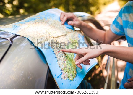 Hands closeup of a young traveler looking at a map while sitting in car trunk