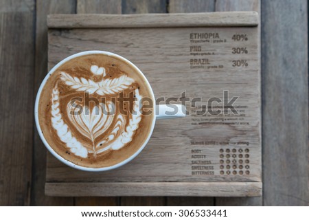 The selective focus picture of a cup of coffee with latte art serves on an old wood plate.\
in vintage look photo.