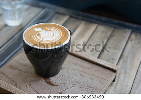 The selective focus picture of a cup of coffee with latte art serves on an old wood plate.\
in vintage style.