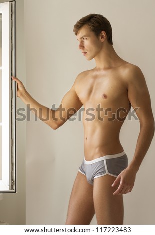 Strong handsome fitness sports man in underwear in bathroom at the window