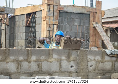 A MALE African construction worker using a Trowel to build a fence on a building site and he is wearing a blue protective helmet and a green reflective traffic jacket to earn a living  ストックフォト © 