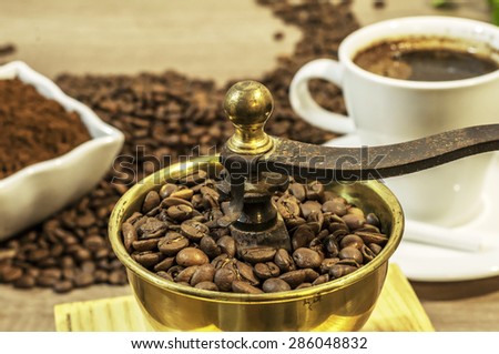 Coffee grinder with coffee beans and ground coffee in bowl on wooden table