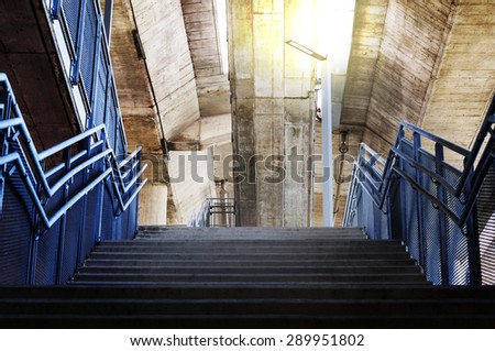 Concrete stairs are metal handrails under the bridge with orange