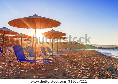Two blue sunbed, straw umbrella on beautiful beach background with burning sun