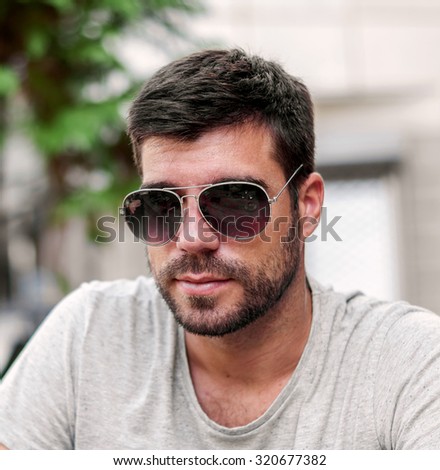 Portrait of a young handsome man, model of fashion, wearing tinted sunglasses in city background