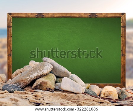 Rock on the beach with green school board picture frame and blurred beach and sea