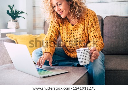 Photo of Nice beautiful lady with blonde curly hair work at the notebook sit down on the sofa at home - check on oline shops for cyber monday sales - technology woman concept for alternative office freelance