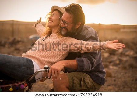 Happy adult people cheerful couple enjoy the outdoor leisure activity riding a bike together man carrying woman and laugh a lot in friendship and relationship - active youthful persons