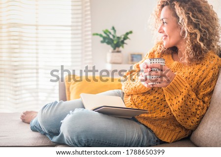Woman have relax at home with cup of tea and book - reading activity for adult beautiful female people - enjoying quiet lifestyle indoor and long blonde curly hair - happy adult female indoor - people