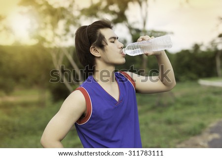 Asians man drinks water from a bottle after running in the park.