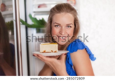 beautiful young woman with a slice of cake at the open fridge