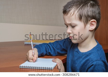 boy student writes in a notebook while sitting at the table