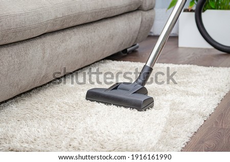 A woman vacuums a gray carpet with a vacuum cleaner. Cleaning and cleanliness concept