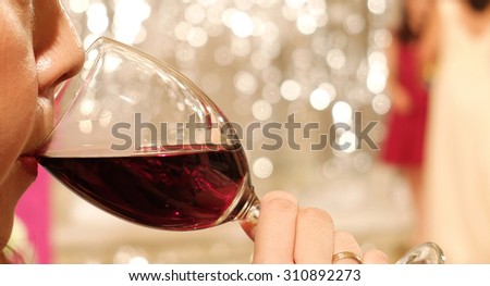 Asian Woman with Lipstick Sipping Red Wine in a Glass at The Corner with Blur Celebration Party in Background