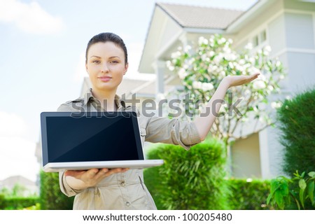 Young businesswoman (real estate agent) holding a laptop and presenting detached family house