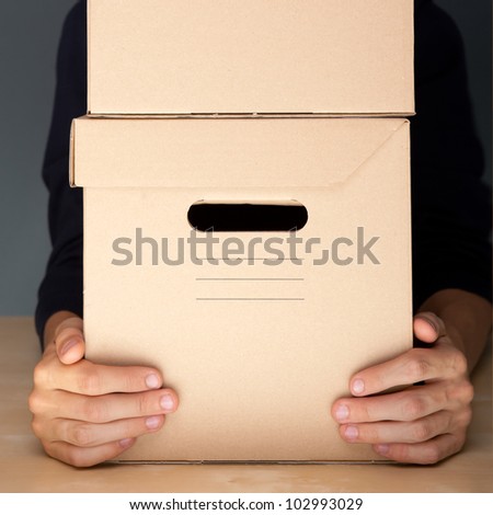 Successful Postal or delivery service concept. Man holding cardboard box with two arms on table