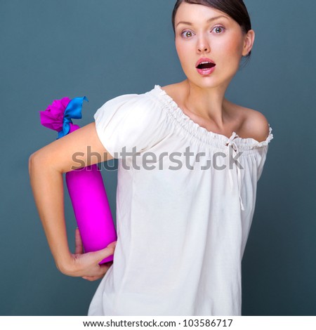 Portrait of young pretty woman holding bottle of prefect wine in gift decorative package against grey background.