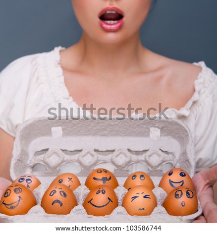 Portrait of young pretty emotional business woman against grey background holding eggs with different emotions on their drawn faces. People management conceptual photo.