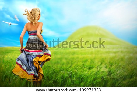 Young woman running across field. Photo from behind. Idyllic scenery and flying birds.