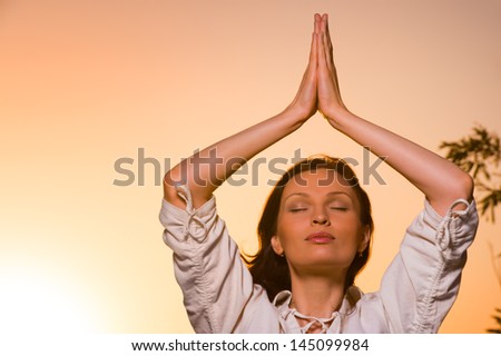 Morning meditation - portrait of young beautiful woman doing yoga against orange sky