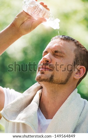 Young sexy male athlete is refreshing himself with water outdoors at summer park