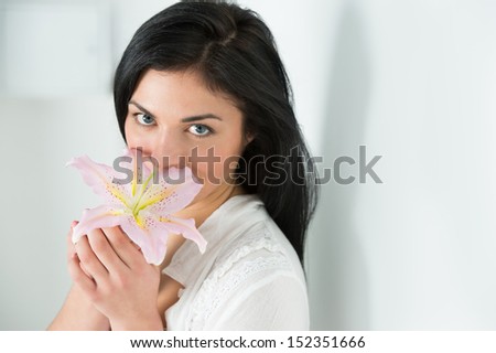 Attractive young woman holding a lily flower in her hand, smelling it\'s perfume against a bright background.