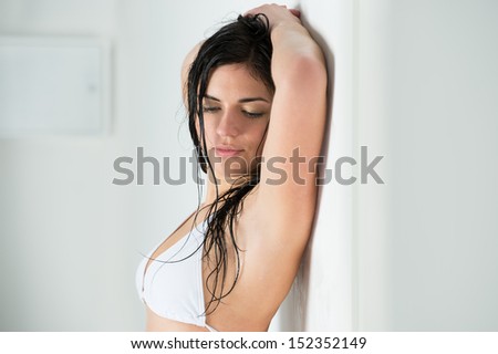 Sexy woman in swimsuit posing at home, leaning on white wall and alluring. Wet hair after shower