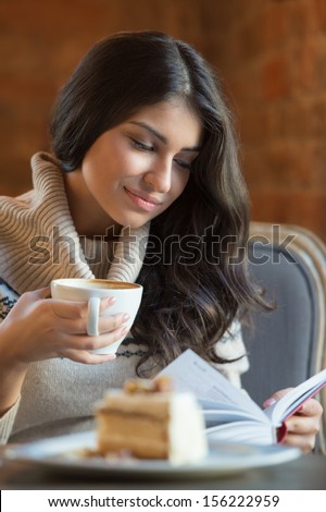 Woman reading a book at cafe while having hot latte coffee and tasty cake