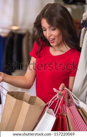 Smiling girl with shopping bags at store looking inside shopping bag