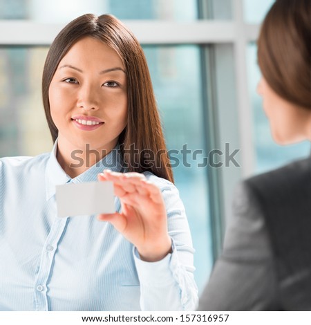 Two successful business women reaching agreement at office and sharing business cards to each other