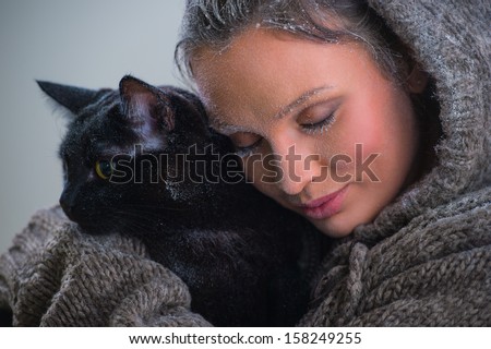 Winter portrait of young kind woman holding big black cat. Frost and snow on them
