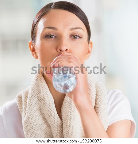 Portrait of young woman drinking water at gym after doing exercises