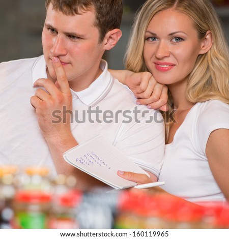 Image of positive couple choosing products in supermarket with list of things to buy
