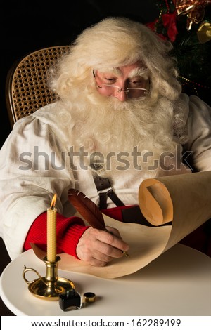 Santa Claus sitting at home and writing on old paper roll to do list with quill pen and ink at night with candle light. Authentic vintage style portrait.